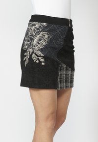 Falda negra que presenta un panel de mezclilla con bordado floral, secciones negras texturizadas y un detalle de cuadros, con cierre lateral con cremallera.