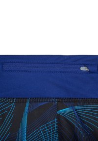 Sininen vyötärönauha vetoketjullisella taskulla, siirtyen mustaan kangasmateriaaliin, jossa on sinisiä abstrakteja viivoja, korostaen sporttista muotoilua.