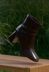 Braune Leder-Ankle-Boots mit glänzender Oberfläche, ausgestattet mit zwei Schnallenriemen und einem klobigen, hohen Absatz. Schlichtes Design und stromlinienförmige Form.