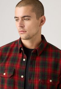 Geruite flanellen shirt met rode, groene en blauwe tinten, knoopsluiting, twee borstzakken en een zachte textuur.