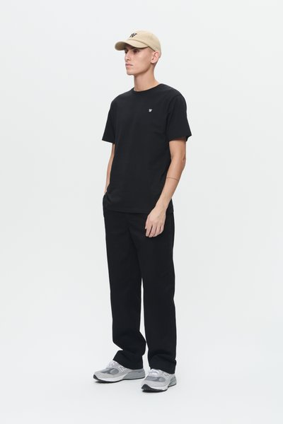 Camiseta negra con pequeño logo, pantalones negros y gorra de color beige claro. Modelo lleva zapatillas de correr grises con acentos blancos y negros.