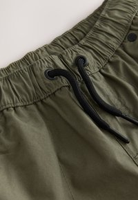 Olive green shorts with an elastic waistband and black drawstrings. Features smooth texture and eyelets for the drawstring.
