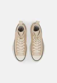 Beige sneakers met een hoge schacht, een bovenwerk van glad leer, een witte rubberen neuskap en gouden oogjes. Voorzien van dikke veters en een lus aan de hiel.