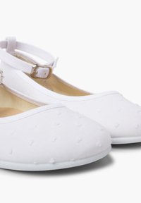 Zapatillas de lona blancas con una textura suave, que presentan una puntera redonda y una correa ajustable en el tobillo. Pequeños puntos elevados decoran la superficie superior.