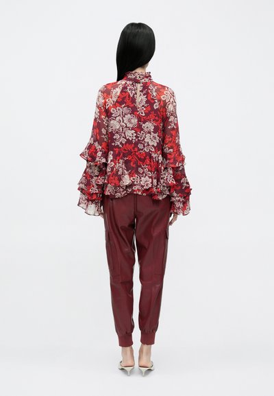 Lilleline, läbipaistev punane pluus volangiliste varrukatega, sobitatud bordoopunaste kitsenevate taskutega pükstega. Komplekti täiendavad kontsakingad.