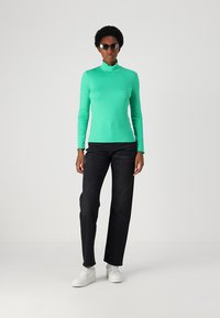 Mint green turtleneck top, fitted design, paired with black straight-leg jeans and white sneakers; sunglasses complete the outfit.