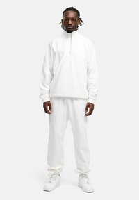 Weiße Zip-Up-Sweatjacke mit lockerer Passform, kombiniert mit passenden Jogginghosen. Glattes Material, gerippte Bündchen und runder Ausschnitt. Weiße Sneaker.