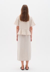 Beige linen mekko, jossa on peplum-vyötärö, lyhyet hihat ja suoraviivainen siluetti. Sileä pinta, nilkkapituinen muotoilu ja yksinkertainen helma. Mustat sandaalit.