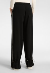 Pantalons de survêtement noirs à coupe lâche, avec des rayures blanches sur les côtés, des poignets resserrés par des cordons de serrage et une texture de tissu lisse.