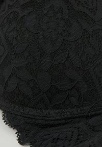 Tel fabricado en encaje negro con un patrón floral, superficie texturizada y borde de encaje con volantes en la parte inferior. Material suave y flexible, con detalles intrincados.