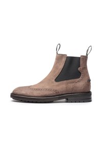 Botín Chelsea de gamuza marrón con paneles laterales de elastano, detalles decorativos de brogue y una suela negra texturizada. Lengüetas en el talón para facilitar el calzado.