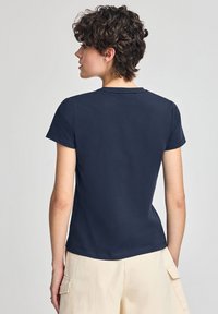 T-shirt in cotone blu navy con una forma aderente, maniche corte e scollatura rotonda, vista dal retro. Texture del tessuto liscia.