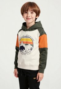 Mikina s kapucí má krémovou barvu těla, zelené rukávy a oranžové akcenty. Obsahuje grafiku s horami a medvědem. Má měkkou texturu a volný střih.