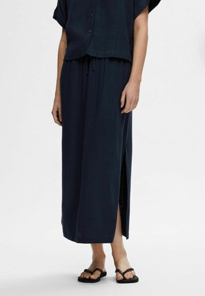 Granatowa sukienka maxi wykonana z lekkiego materiału, o luźnym kroju, z krótkimi rękawami i bocznym rozcięciem dla większej swobody ruchów.