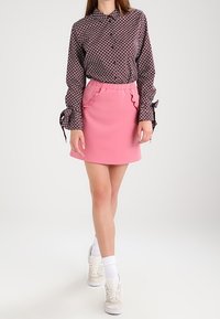 Långärmad skjorta med ett svart och vitt mönster, parat med en pink mini kjol med volangdetaljer. Bärs med vita strumpor och sneakers.