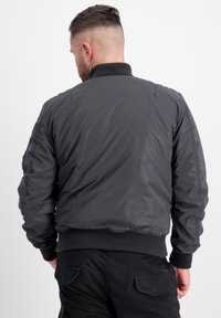 Giacca bomber grigia scura con colletto e polsini a costine, dotata di un'esterno liscio e lucido e di una vita elasticizzata.