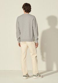 Sudadera gris claro con cuello redondo y puños acanalados, combinada con pantalones color crema y zapatillas blancas con detalles grises.