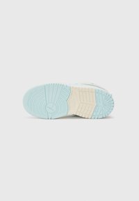 Semelle de chaussure avec une bande de roulement bleu clair et beige comportant des motifs circulaires et en grille, incluant un petit logo Jumpman embossé près de la zone des orteils.