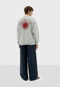 Sudadera gris con un gráfico de un sol rojo y texto en la parte de atrás, combinada con pantalones navy holgados. La tela parece suave y casual.