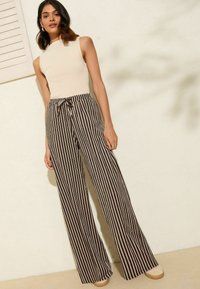 Top sin mangas de color beige combinado con pantalones anchos de tiro alto en rayas marrones y blancas que cuentan con una cintura con cordón. Textura suave y ajuste holgado.