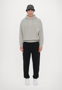 Hanorac gri cu șnururi și buzunar frontal, asociat cu pantaloni de trening negri. Adidași albi completează ținuta. Design simplu, fără tipare.