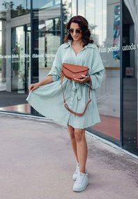 Svetle zelené, strukturované šaty na knoflíky s páskem na zavázání, kombinované s bílými teniskami a hnědou crossbody taškou s prohnutým překlápěcím víkem.