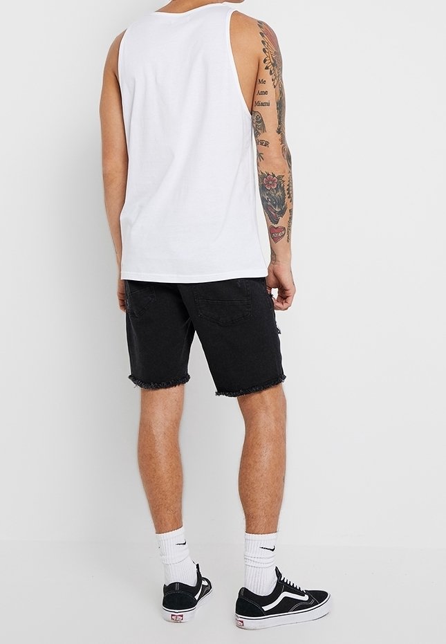 Biała bezrękawnik, czarne szorty dżinsowe z postrzępionymi końcami, zestawione z białymi skarpetkami i czarnymi trampkami. Tatuaże widoczne na ramieniu.