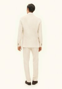 Licht beige linnen pak met een getailleerde pasvorm, colbert met twee knopen en rechte broekspijpen, met een subtiele textuur en drieknopen manchetten als accenten.