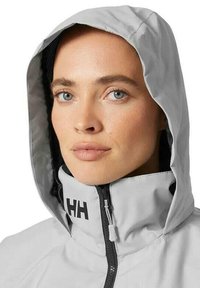 Light gray hooded jacket with a high collar, featuring a black logo on the zipper flap and a smooth, water-resistant texture.