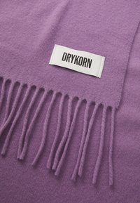 Sciarpa di lana viola con bordi frangiati e un'etichetta di stoffa bianca con la scritta "DRYKORN" in lettere nere. Texture morbida e liscia.