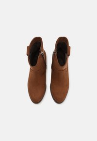 Bottes chevilles en daim marron avec fermetures éclair sur les côtés, bouts ronds et languettes à l'arrière pour un enfilage facile. Texture lisse sur l'ensemble.