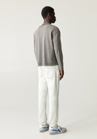 Grijze langslavige shirt gecombineerd met witte jeans en grijze sneakers. Het shirt heeft een ontspannen pasvorm; de jeans hebben achterzakken en lichte slijtagesporen.