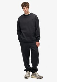Sudadera y pantalones de color gris oscuro fabricados en una mezcla de algodón. Corte relajado con puños acanalados y un pequeño logo en el pecho. Calzado casual.