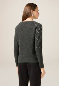 Grauer Pullover mit einem strukturierten Strickdesign, verziert mit kleinen glänzenden Akzenten an den Schultern und langen Ärmeln.