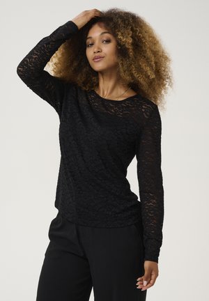 Black lace long-sleeve top with a round neckline, featuring a textured floral pattern and a fitted silhouette, paired with black trousers.