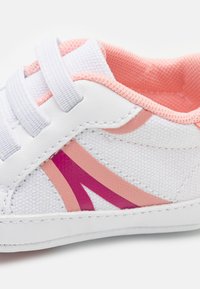 Weiße Sneakers mit rosa und lila Akzenten. Verfügt über ein strukturiertes Obermaterial, elastische Riemen und ein gepolstertes Innenfutter. Rundliche Zehenpartie.