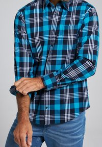 Blå och svart rutiga skjorta med långa ärmar, knappad krage och fickdetalj. Tyget verkar slätt och lätt.