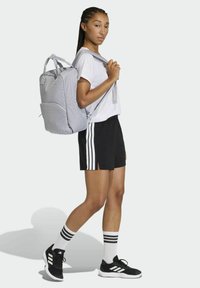 Light gray backpack with front pocket, black shorts with white stripes, white t-shirt, black athletic shoes with white accents, striped socks.