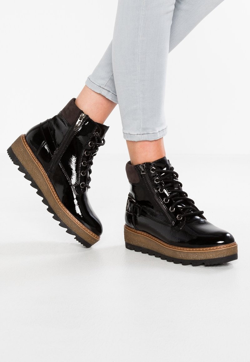 Bottines en cuir verni noir avec une semelle plateforme texturée beige, lacets à l'avant et fermeture éclair sur le côté. Semelle extérieure en caoutchouc avec motif en zigzag.