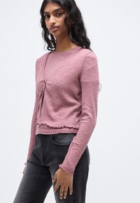 Κοντομάνικη, ριμπ πλεκτή μπλούζα σε αποχρώσεις του μωβ με cropped σχεδιασμό, που διαθέτει κουμπιά μπροστά και τελείωμα με ξεφτισμένες άκρες. Συνδυάζεται με σκουρόχρωμο τζιν.