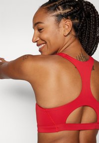 Sujetador deportivo rojo con diseño de espalda nadadora, que presenta detalles recortados y costuras planas para mayor comodidad. Fabricado con tejido elástico para ropa activa.