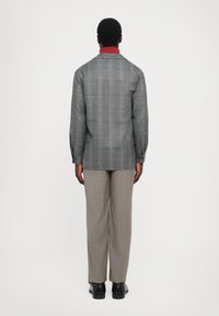 Hallikaelusega hall ruuduline särk-jakk, mis on kombineeritud heledate hallide pükstega, vaatatuna tagant. Sile tekstuur, mugav lõige ja lihtne disain.