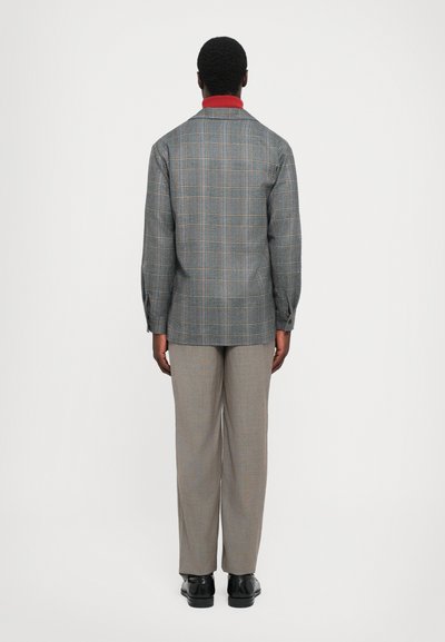 Hallikaelusega hall ruuduline särk-jakk, mis on kombineeritud heledate hallide pükstega, vaatatuna tagant. Sile tekstuur, mugav lõige ja lihtne disain.