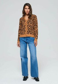 Cardigan à imprimé léopard en beige et noir, avec un col en V, une fermeture à boutons et des poignets côtelés, associé à un jean large bleu clair.