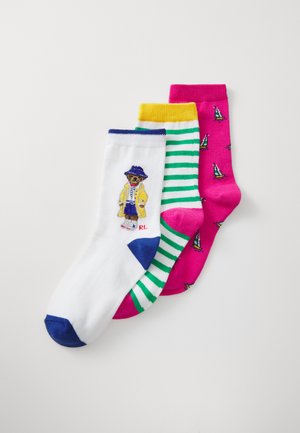 Trois paires de chaussettes en coton : blanches avec un bout bleu et un motif d'ours, rayées vertes avec des accents jaunes, et roses avec un petit motif de bateau à voile.