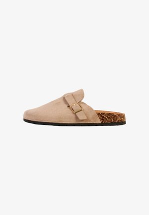Beige ruskind slip-on træsko med justerbar spænde, korkfodtøj og sort gummisål, vist fra siden.