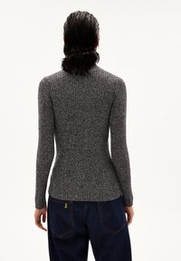 Suéter de manga larga acanalado en gris oscuro, con un cuello alto. Combinado con jeans azul oscuro, costuras visibles y un detalle amarillo en el bolsillo.