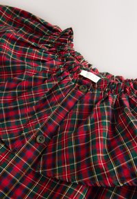 Chemise à carreaux rouges et verts avec un col froncé. Dotée de boutons et d'un tissu doux et texturé. Étiquette visible près du col.