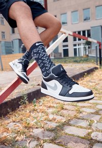 Zapatillas Nike Air Jordan en blanco y negro con parte superior de cuero suave, punta perforada, suela texturizada y detalle de swoosh gris.