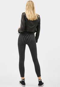 Černá kožená krátká bunda spojená s přiléhavými černobílými pruhovanými kalhotami. Má zadní kapsy a vysoký pas.